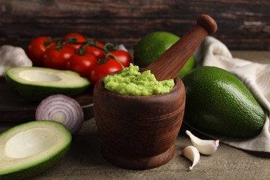 Mortar with delicious guacamole and ingredients on wooden table