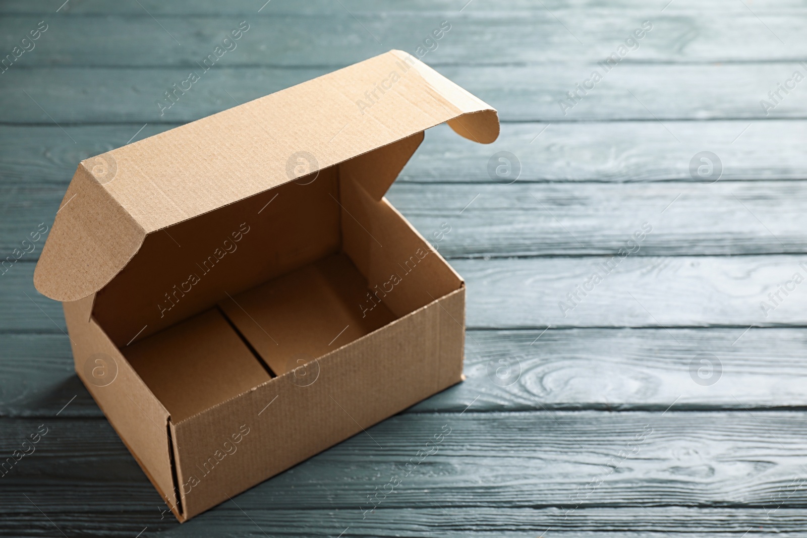 Photo of Open cardboard box on dark wooden table. Space for text