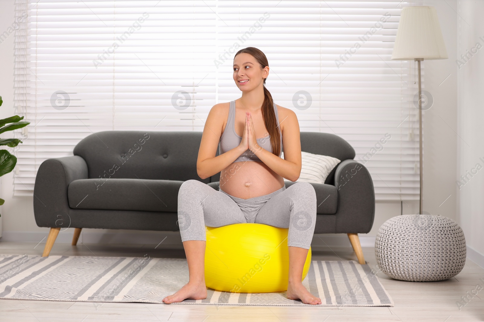 Photo of Pregnant woman meditating on fitness ball in room. Home yoga