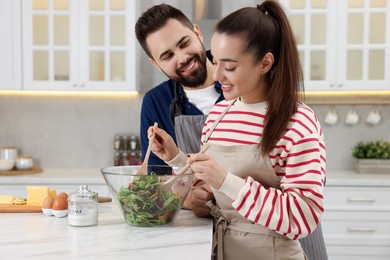 Happy affectionate couple cooking together at white table in kitchen