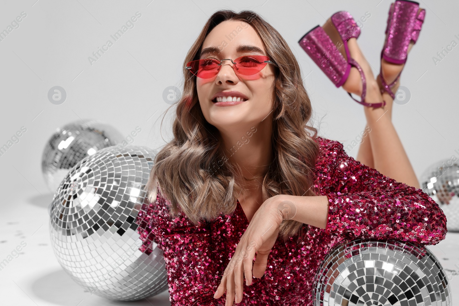 Photo of Beautiful woman in sunglasses and sequin dress among disco balls on white background