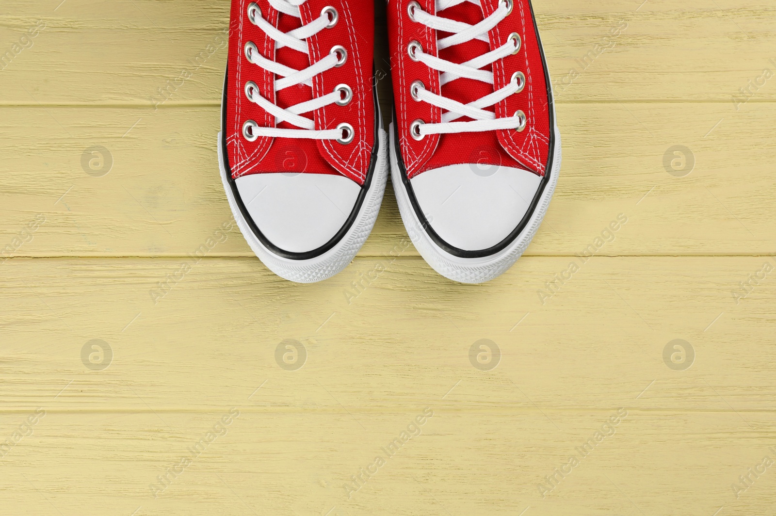 Photo of Pair of red sneakers on yellow wooden table, flat lay. Space for text
