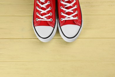 Photo of Pair of red sneakers on yellow wooden table, flat lay. Space for text