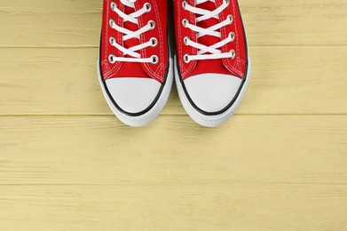 Pair of red sneakers on yellow wooden table, flat lay. Space for text