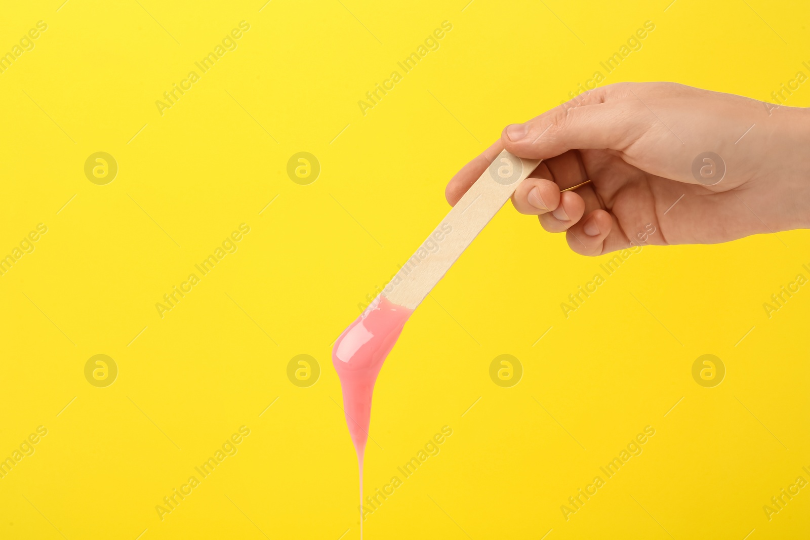 Photo of Woman holding spatula with hot depilatory wax on yellow background, closeup