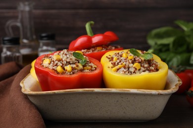 Photo of Quinoa stuffed bell peppers and basil in baking dish on table, closeup