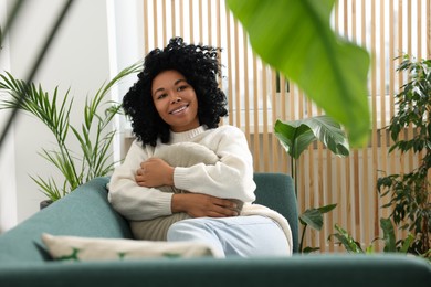 Photo of Happy woman relaxing on sofa near beautiful houseplants at home
