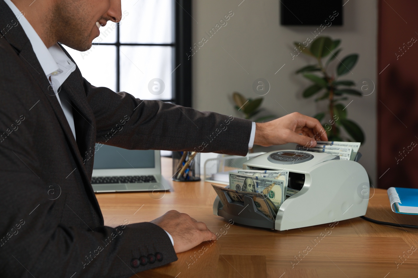 Photo of Man putting money into banknote counter at wooden table indoors, closeup