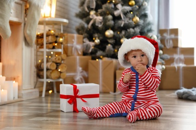 Photo of Little baby with Santa hat and Christmas gift on floor at home