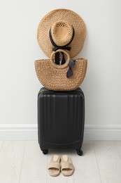 Suitcase packed for trip, shoes and summer accessories near white wall indoors