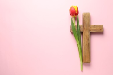 Easter - celebration of Jesus resurrection. Wooden cross and tulip on pink background, top view. Space for text