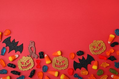 Photo of Tasty candies and Halloween decorations on red background, flat lay. Space for text