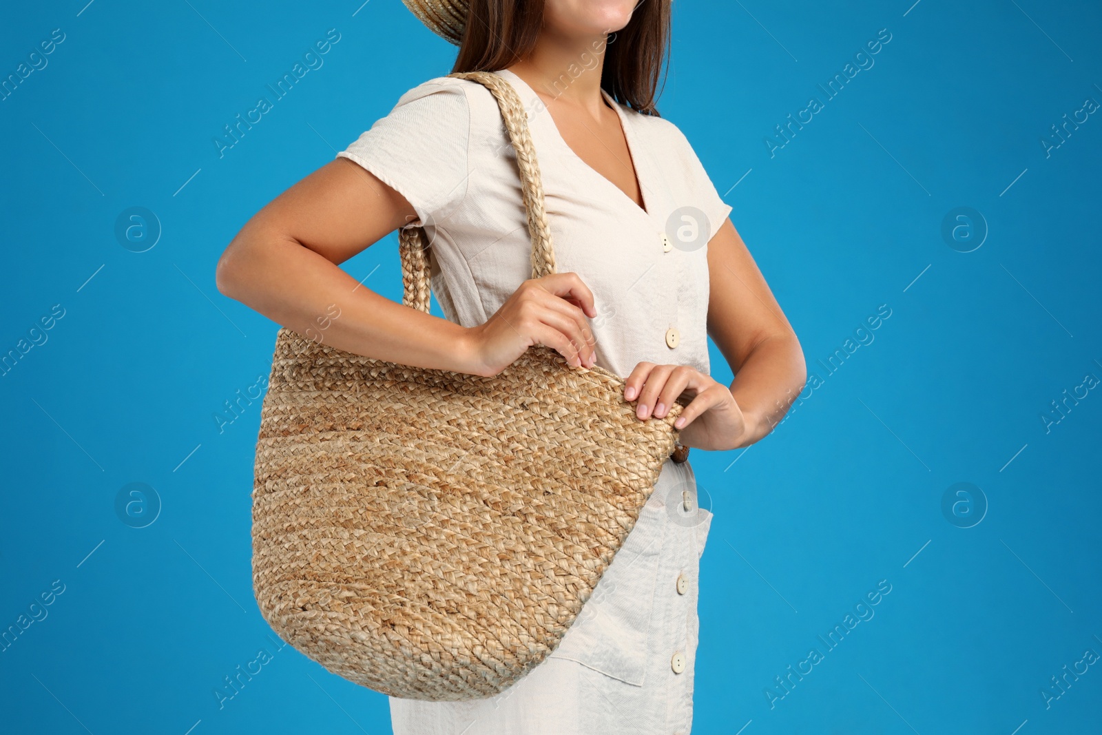 Photo of Young woman with stylish straw bag on light blue background, closeup