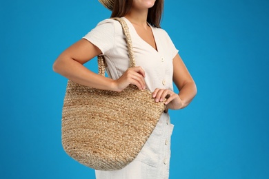 Young woman with stylish straw bag on light blue background, closeup