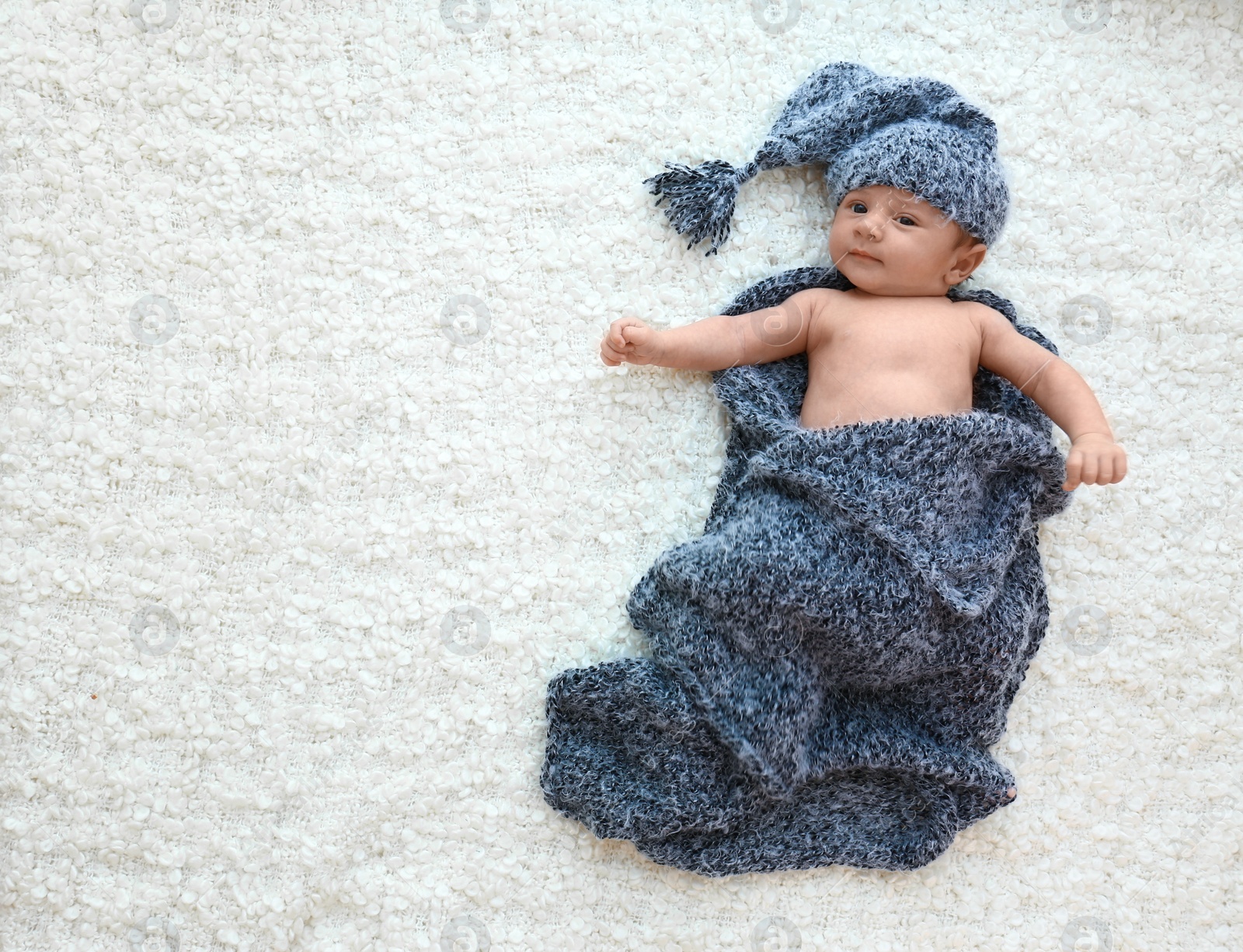 Photo of Cute little baby in grey hat and plaid lying on soft blanket, top view. Space for text