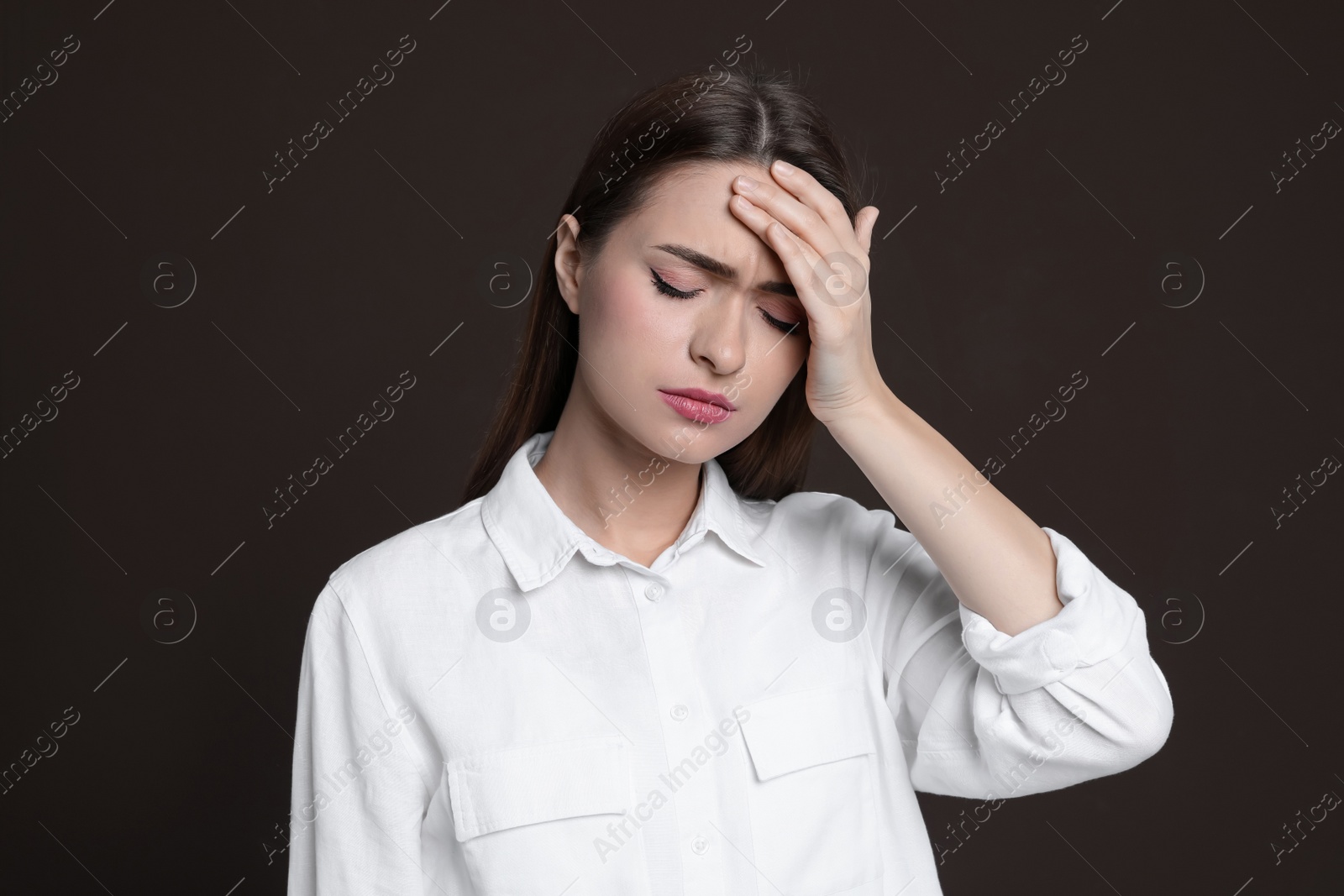 Photo of Young woman suffering from headache on brown background