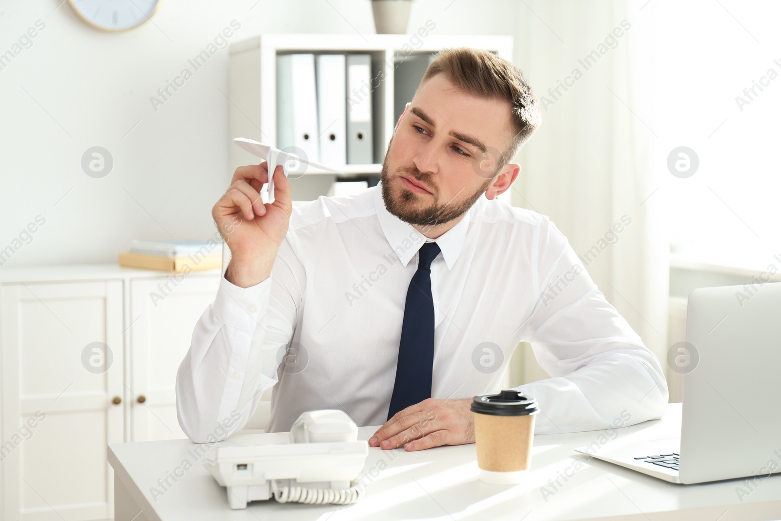 Photo of Lazy young man playing with paper plane at workplace