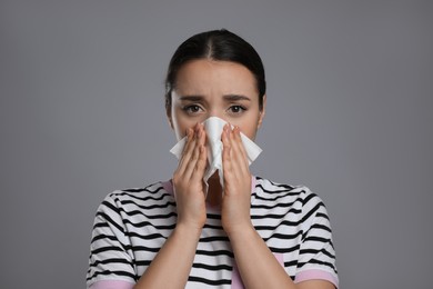 Photo of Young woman blowing nose in tissue on grey background. Cold symptoms