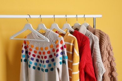 Photo of Collection of warm sweaters hanging on rack against color background