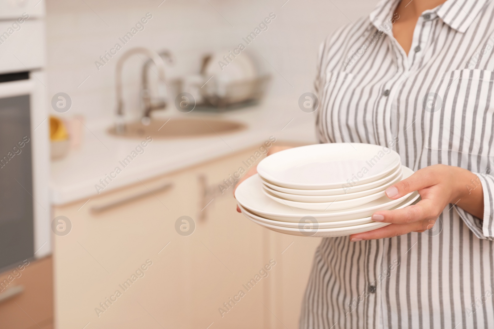 Photo of Woman holding stack of clean dishes in kitchen. Space for text