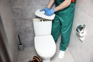 Photo of Plumber repairing toilet bowl in water closet, closeup