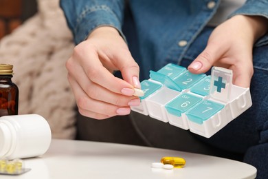 Photo of Woman taking pill from plastic container at white table indoors, closeup