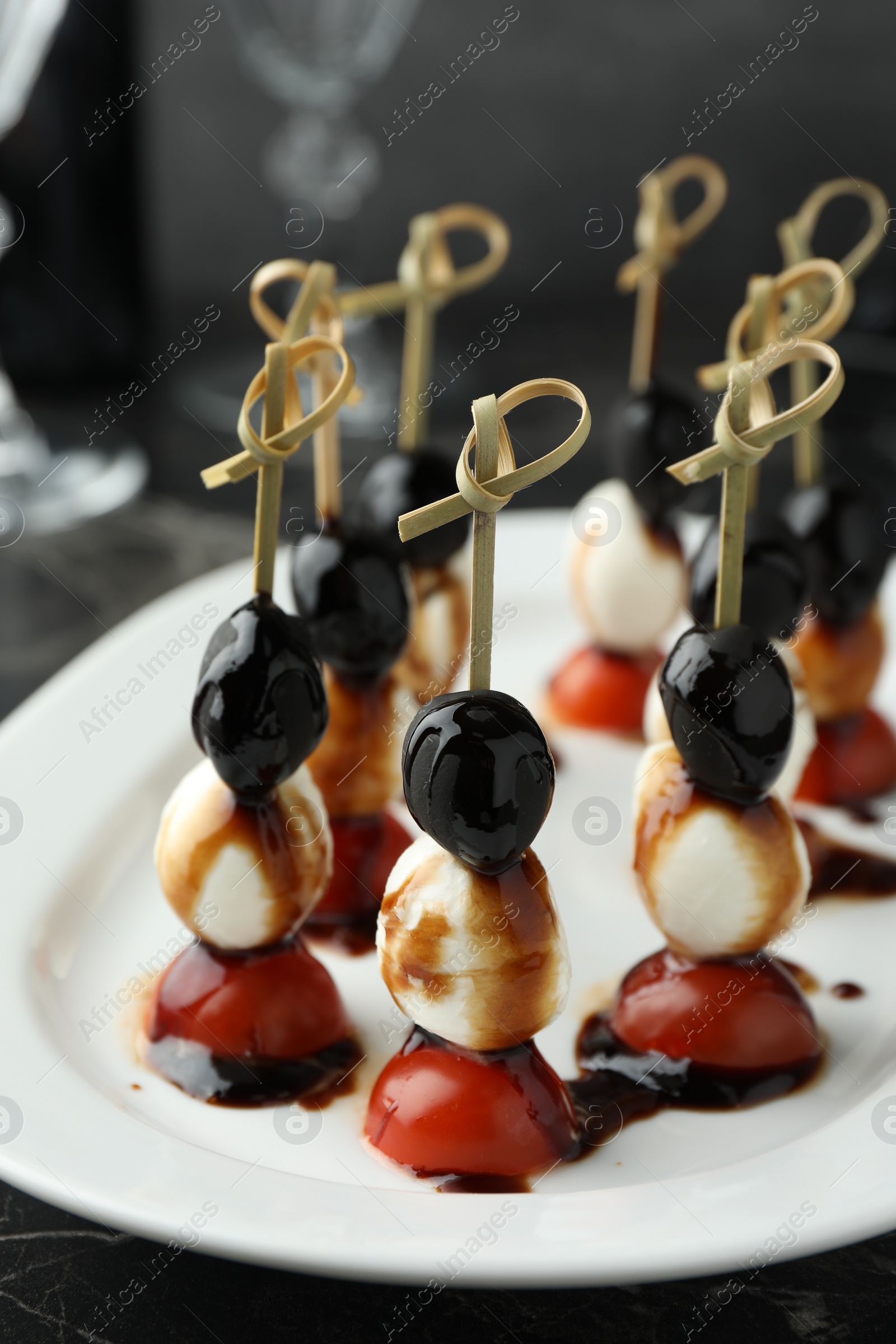 Photo of Tasty canapes with black olives, mozzarella and cherry tomatoes on dark textured table, closeup