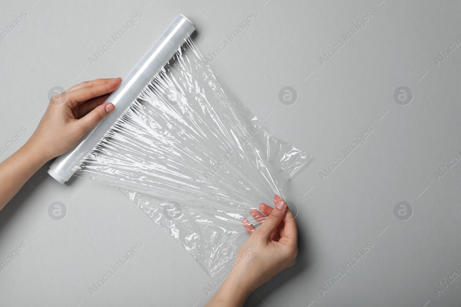 Photo of Woman with roll of stretch wrap on grey background, top view