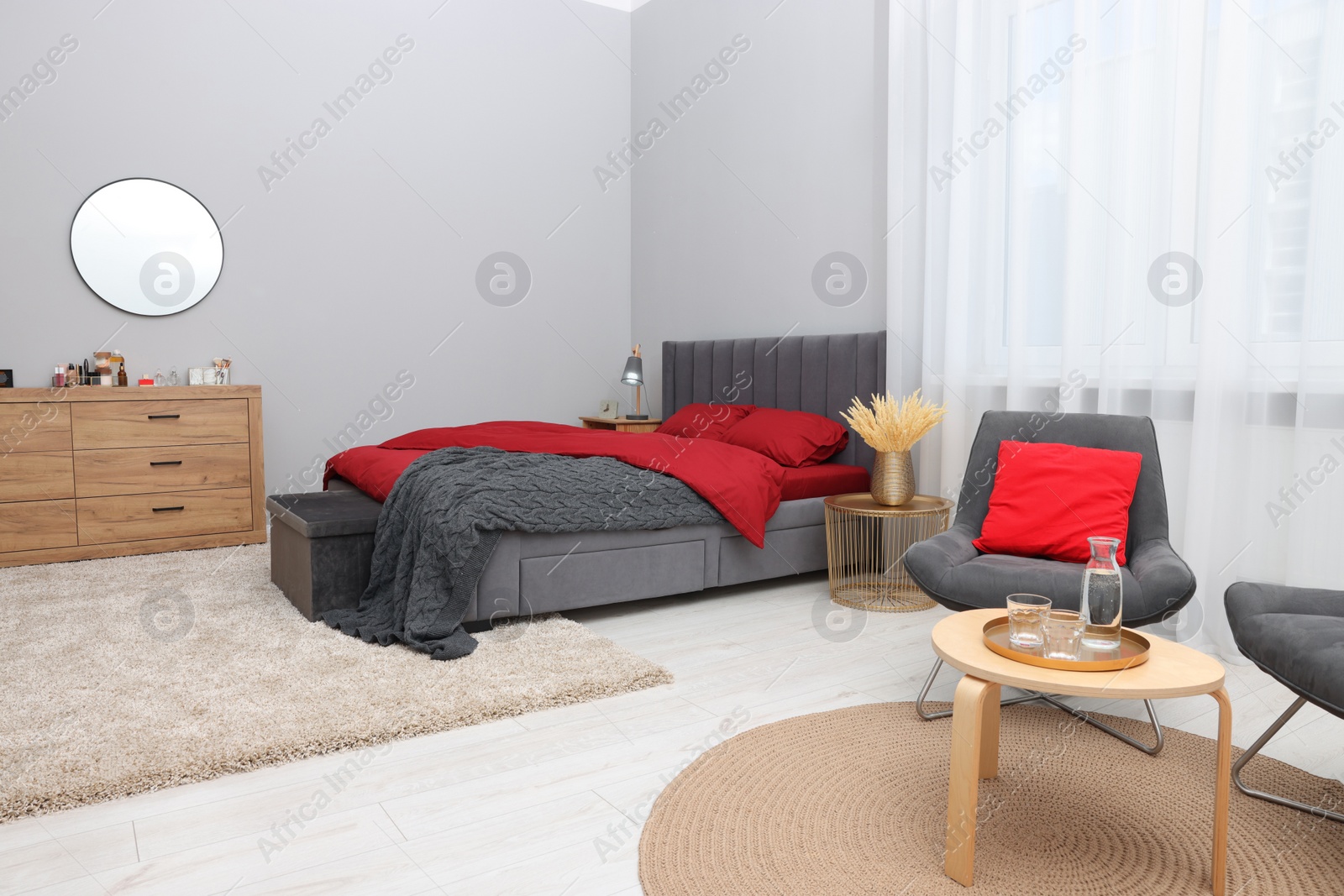 Photo of Stylish bedroom with comfortable bed, armchair, table and wooden chest of drawers. Interior design