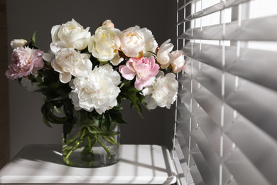Photo of Beautiful peonies in vase on table near window indoors