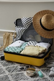 Photo of Open suitcase with summer clothes and accessories near white wall indoors