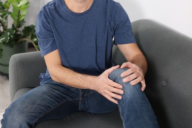 Photo of Man suffering from leg pain and touching knee on sofa indoors, closeup