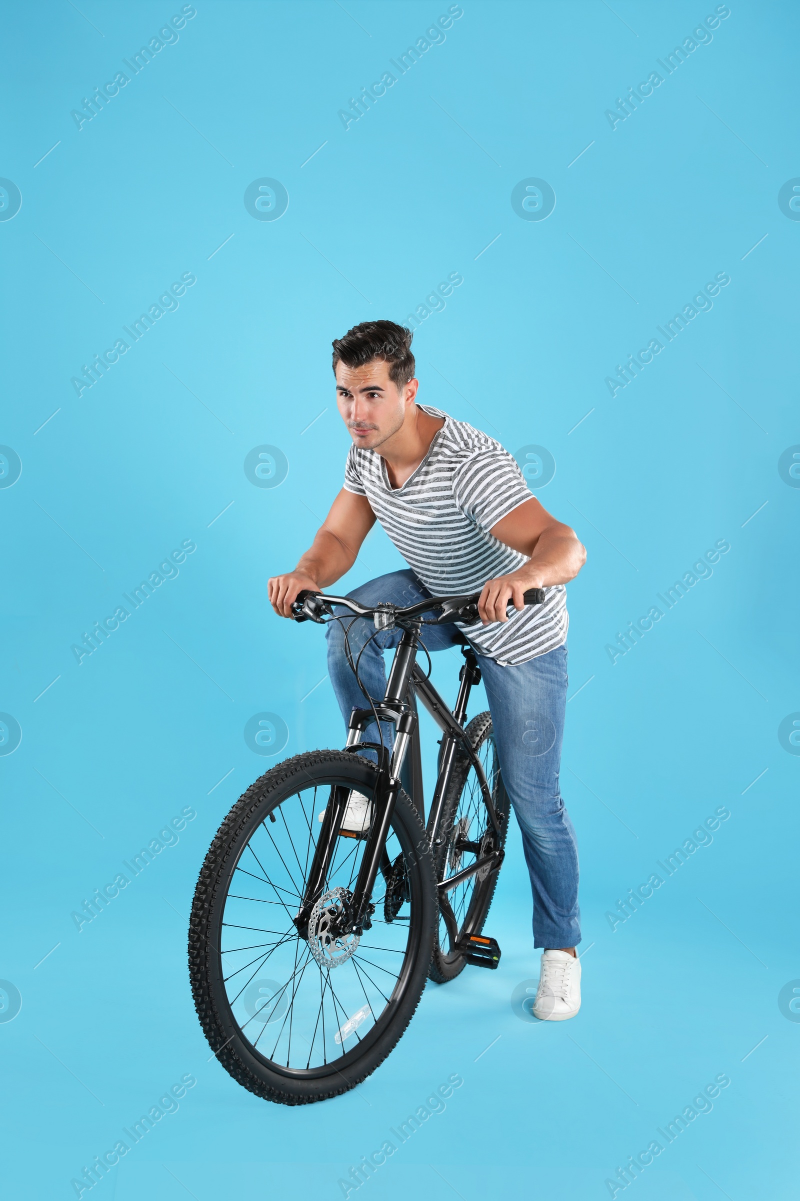 Photo of Handsome young man with modern bicycle on light blue background