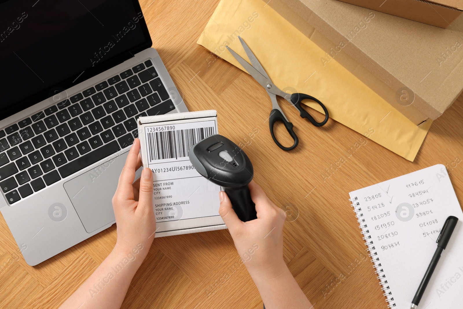 Photo of Woman with scanner reading parcel barcode at wooden table, top view. Online store