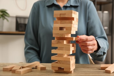 Photo of Playing Jenga. Woman removing block from tower at wooden table indoors, closeup