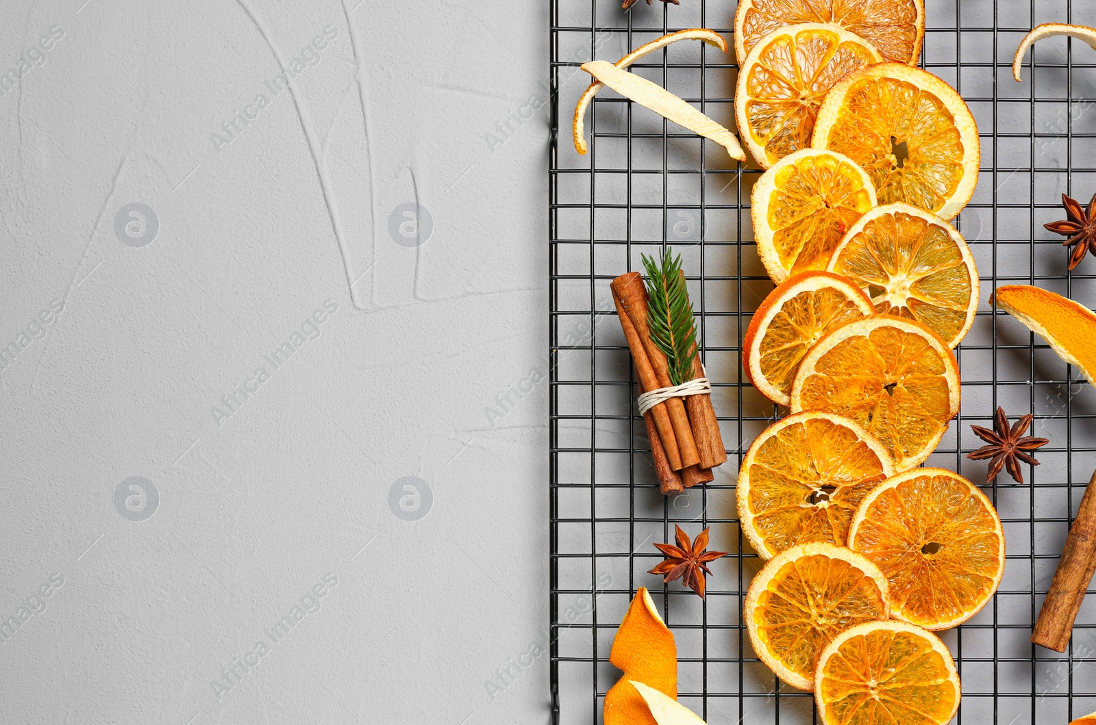 Photo of Flat lay composition with dry orange slices, anise stars and cinnamon sticks on light grey table. Space for text