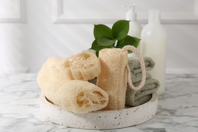 Loofah sponges, towels, green leaves and cosmetic products on white marble table