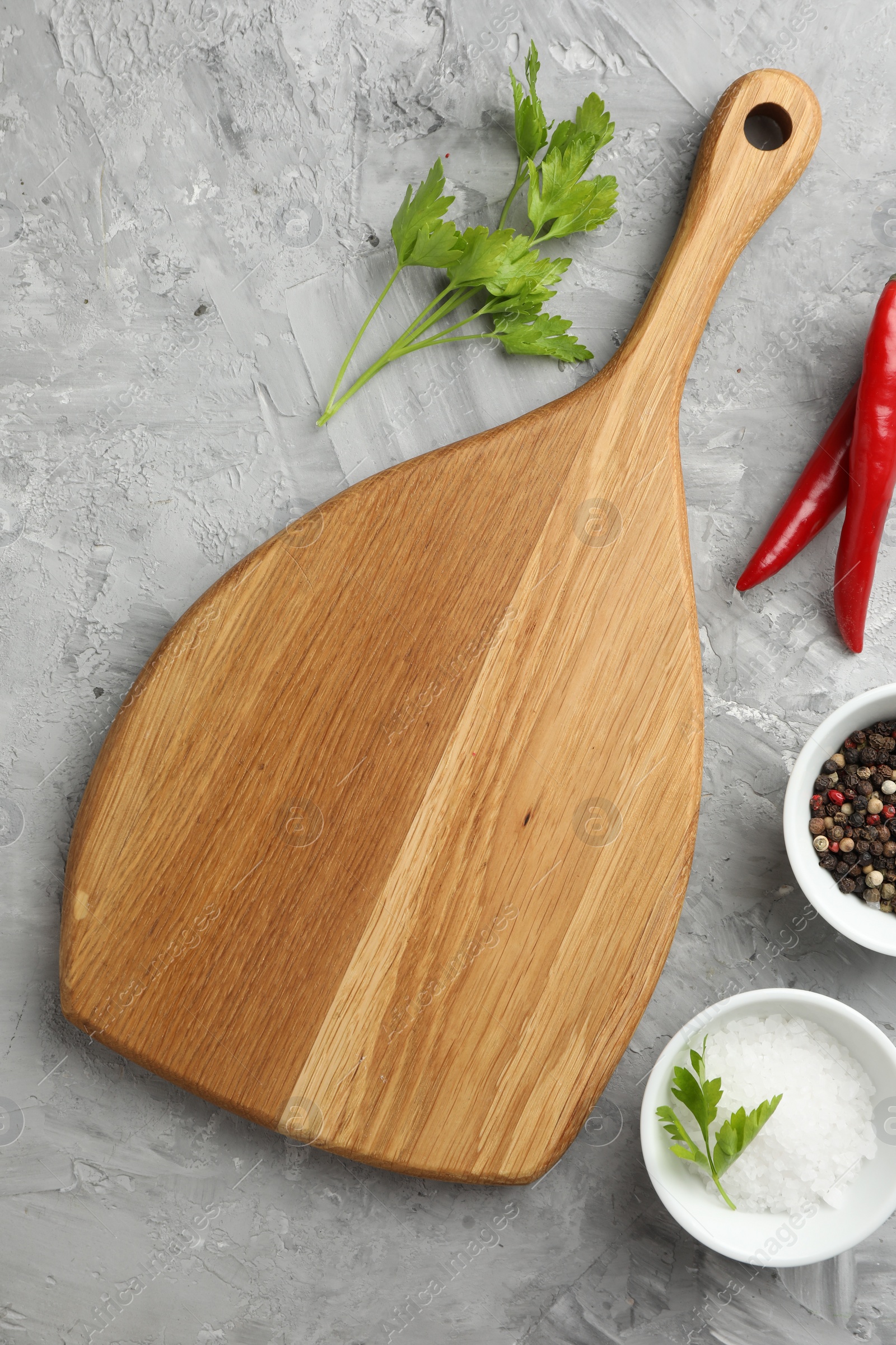 Photo of Cutting board, salt, spices, chili peppers and parsley on grey textured table, flat lay. Space for text