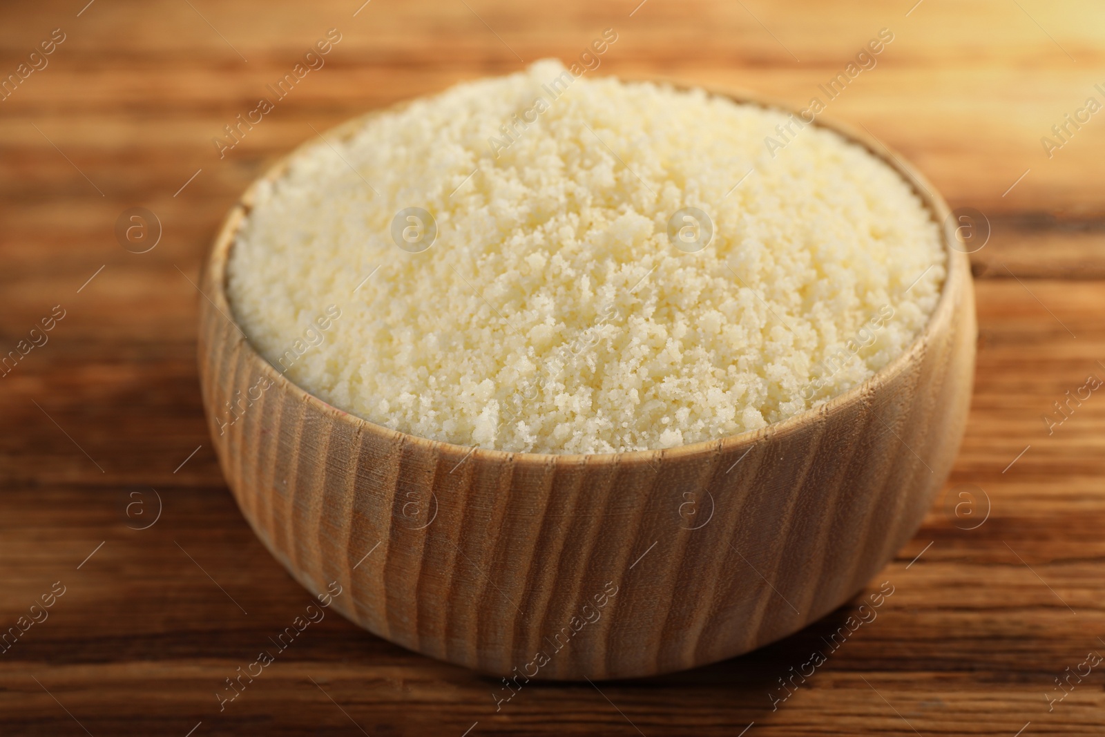 Photo of Bowl with grated parmesan cheese on wooden table, closeup