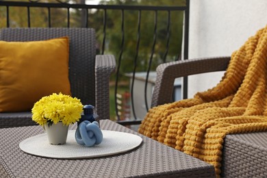 Photo of Orange pillow, soft blanket and yellow chrysanthemum flowers on rattan garden furniture outdoors