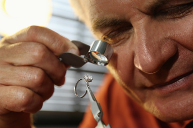 Photo of Professional jeweler evaluating beautiful ring in workshop, closeup