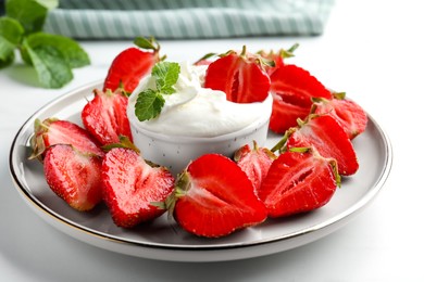 Delicious strawberries with whipped cream on white table, closeup