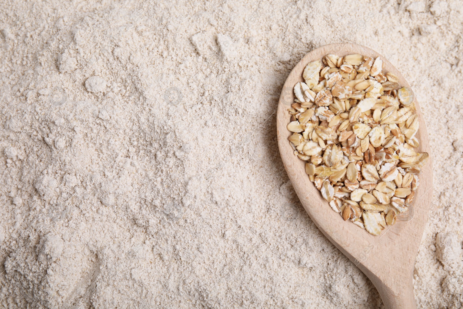 Photo of Spoon with oat flakes on flour, top view. Space for text