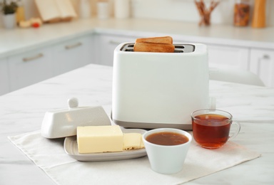 Photo of Modern toaster with bread slices, jam and butter on white marble table in kitchen