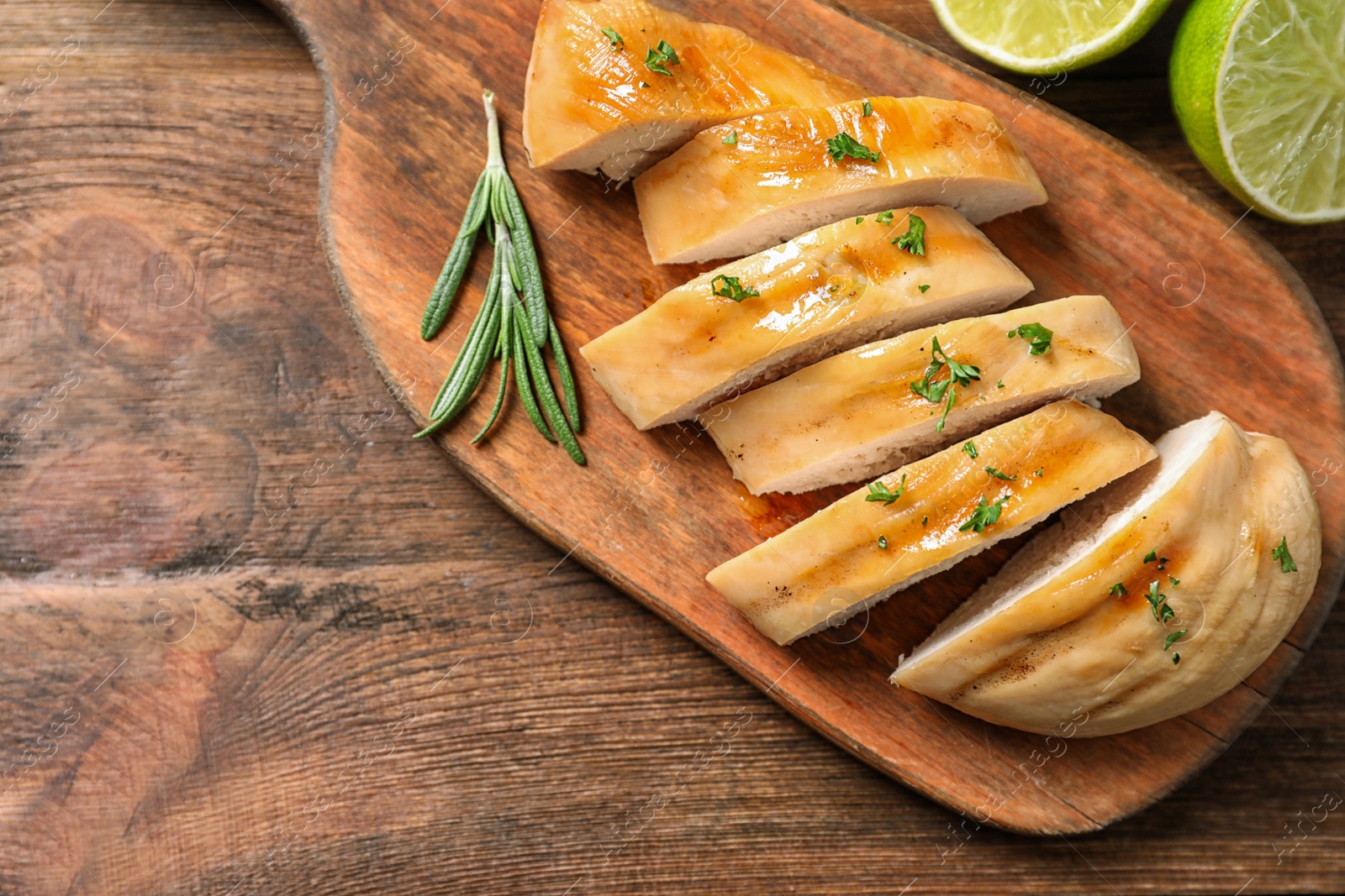 Photo of Board with fried chicken breast and limes on wooden background, top view. Space for text