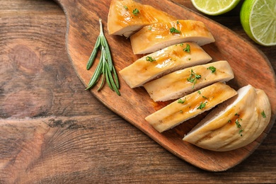 Photo of Board with fried chicken breast and limes on wooden background, top view. Space for text