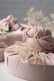 Photo of Furoshiki technique. Gifts packed in pink fabric and dried branches on white table, closeup