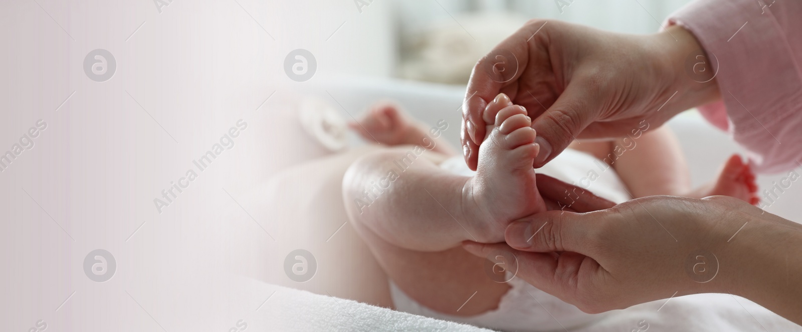 Image of Mother massaging her cute baby with oil on changing table, closeup. Banner design with space for text