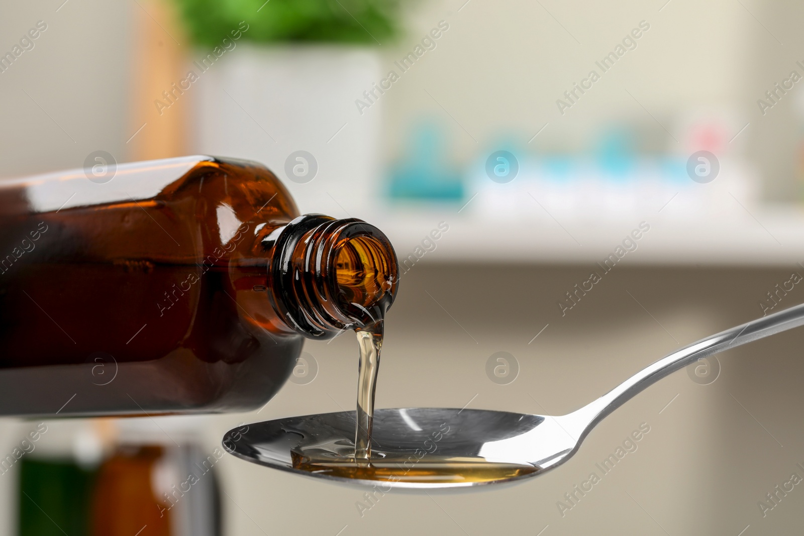 Photo of Pouring syrup from bottle into spoon against blurred background, closeup. Cold medicine