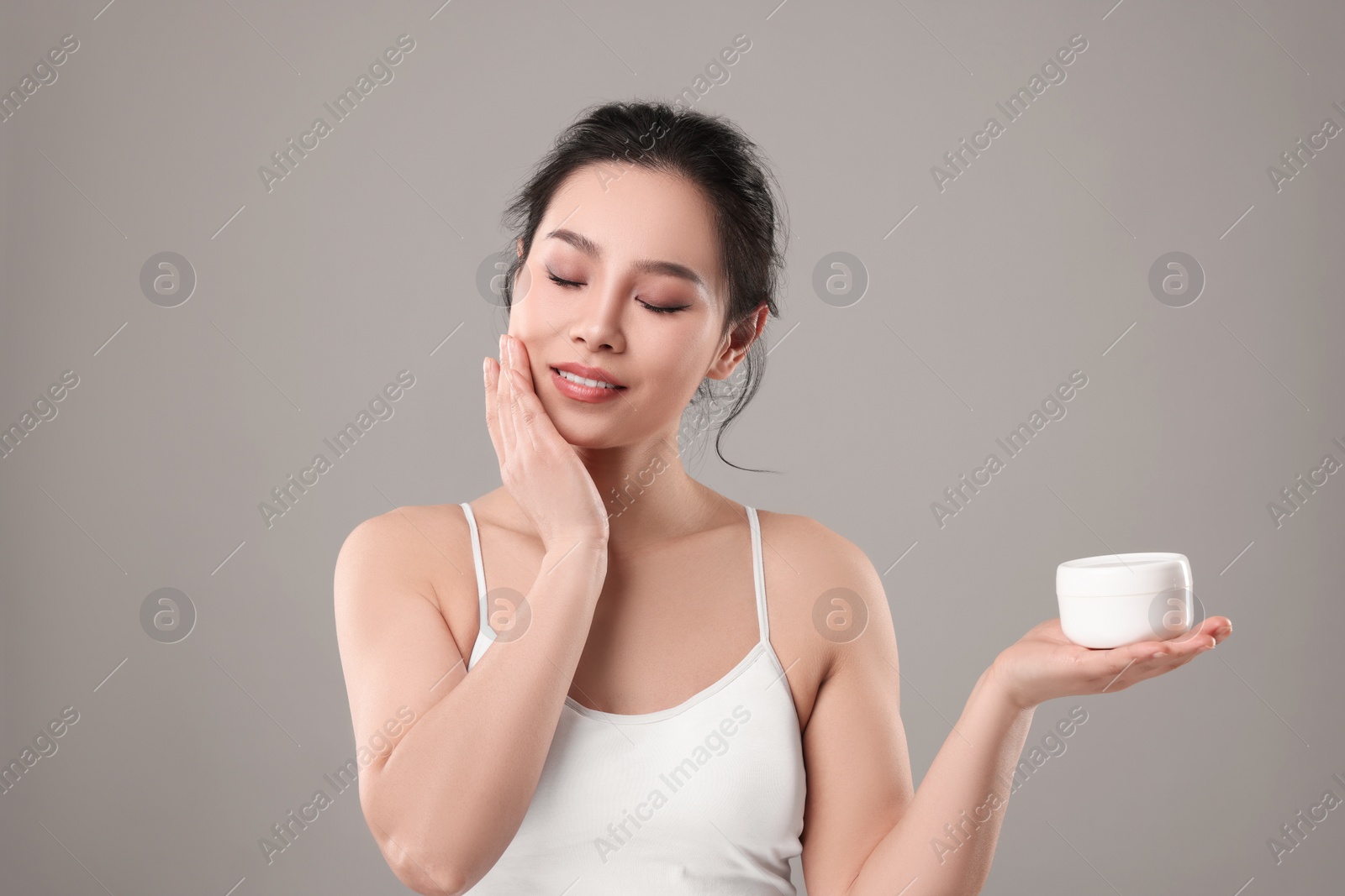 Photo of Happy woman applying face cream on grey background